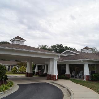 A building with a covered entrance and circular driveway surrounded by landscaping.