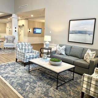 A modern living room featuring a comfortable sofa, a coffee table, and stylish armchairs with patterned fabric. The room is adorned with a decorative carpet and a large framed artwork on the wall.