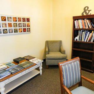 A cozy waiting room with a bookshelf, chairs, and magazines on a table.