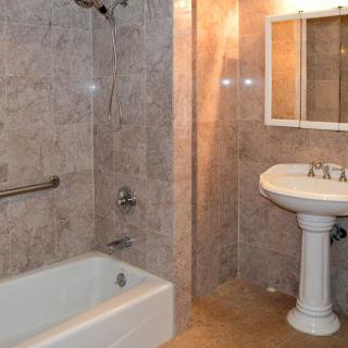A bathroom with tiled walls, featuring a bathtub, pedestal sink, and mirror.