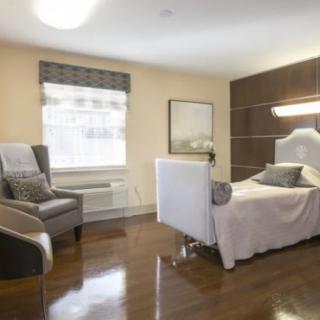 A modern and elegantly furnished bedroom with a comfortable bed, cushioned chair, and large window.