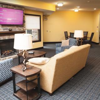 A cozy living room with a yellow couch, television, and fireplace, adjacent to a dining area.