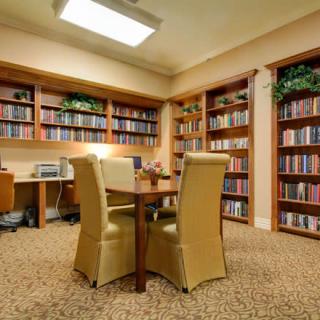 A cozy library room with shelves filled with books, a central table, and comfortable chairs.