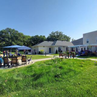 A sunny day with people enjoying a patio area next to a building, surrounded by lush grass and trees.