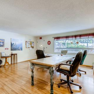 A bright office space with wooden flooring, featuring a large window, several chairs, and a spacious desk.