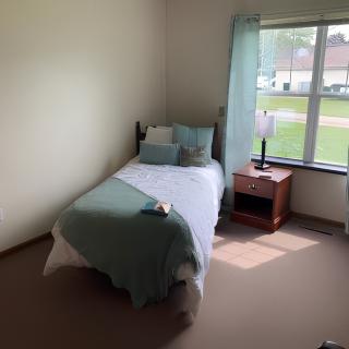 A minimalist bedroom with a single bed, nightstand, and sunlight streaming through the window.