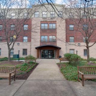 A residential apartment building with a landscaped pathway and benches leading to the entrance.