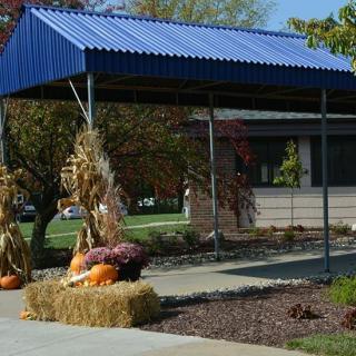 A seasonal outdoor display with hay bales and pumpkins under a blue canopy.