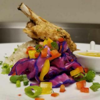 A gourmet dish featuring a lamb shank with vibrant purple cabbage salad and colorful diced vegetables.