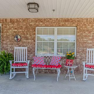A cozy front porch with rocking chairs and decorative cushions against a brick wall.