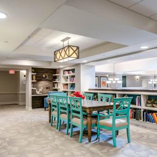 A modern dining area with turquoise chairs and a stylish chandelier, complemented by surrounding bookshelves.