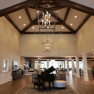A spacious and elegantly designed living room featuring high ceilings, wooden beams, and a grand piano.