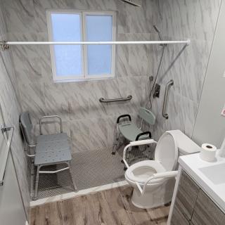 A modern, accessible bathroom featuring a walk-in shower with grab bars and a mobility aid chair.