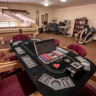 A cozy room with a poker table set up for a game night, featuring casino chips and surrounded by comfortable seating. Exercise equipment can be seen in the background.