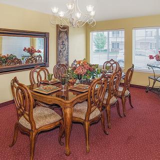 A well-furnished dining room with a large wooden table, surrounded by chairs, under a chandelier.