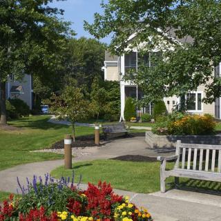 A peaceful garden scene with benches, flowers, and a house in the background.