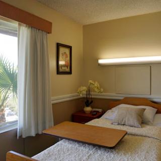 A spacious hospital room featuring two beds, a window with curtains, and warm decor.