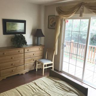 A cozy bedroom featuring a wooden dresser, chair, and lamp near a sliding glass door with curtains.