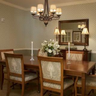 A cozy dining room with a wooden table, elegantly decorated with candles and flowers, under a classic chandelier.