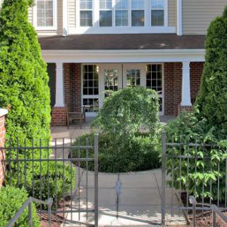 A welcoming building entrance surrounded by lush greenery and a decorative fence.