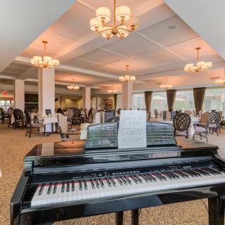 A grand piano in an elegantly furnished dining lounge with chandeliers and seating arrangements.