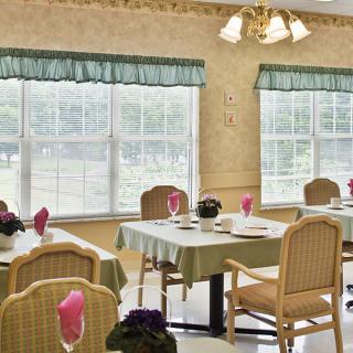 A well-lit dining room with neatly arranged tables and chairs, featuring large windows and decorative accents.
