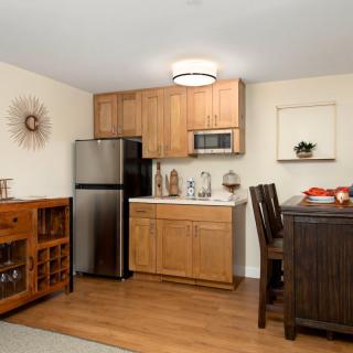 A modern kitchen interior with wooden cabinets, featuring a refrigerator, microwave, and dining area.