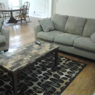 A cozy living room featuring a gray sofa and armchair, a patterned rug, and a wooden coffee table.
