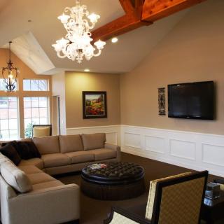 A stylish living room featuring a modern chandelier, large sofa, and wall-mounted TV with exposed wooden beams on the ceiling.