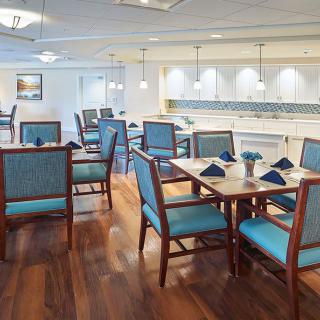 A well-lit dining area with neatly arranged tables and chairs on a wooden floor.
