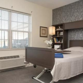 A well-furnished hospital room with a bed, bookshelf, and large window.