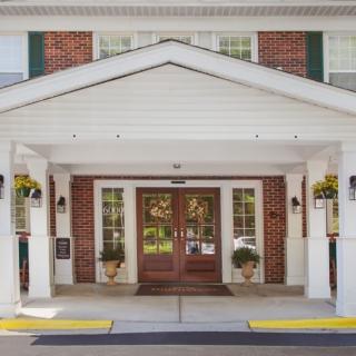 A welcoming building entrance with a brick facade and white columns adorned with hanging plants.