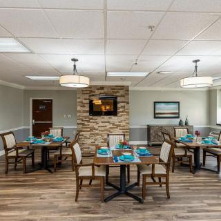 A cozy dining room featuring several tables and chairs, with a warm atmosphere enhanced by wood flooring and ambient lighting.