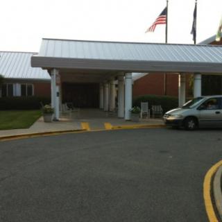 A building entrance with a car parked under an awning and flags flying in the background.