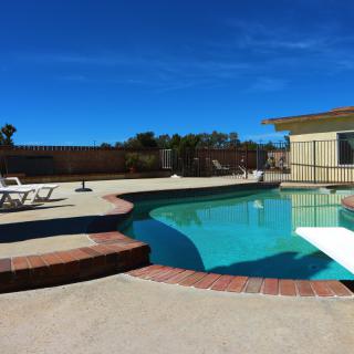 A sunny backyard with a swimming pool and diving board, surrounded by patio furniture.