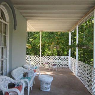 A scenic porch with wicker furniture and hanging plants, overlooking lush greenery.