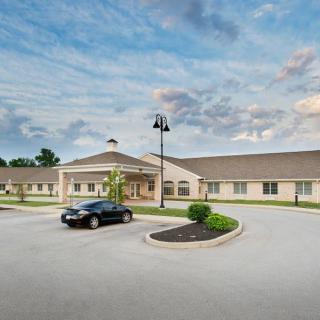 A single-story building with a parking lot and a car parked in front, set against a cloudy sky backdrop.
