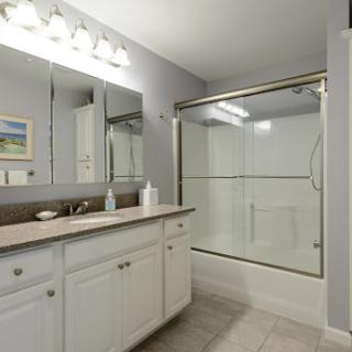 A modern and clean bathroom featuring a glass shower, white cabinetry, and ample lighting.