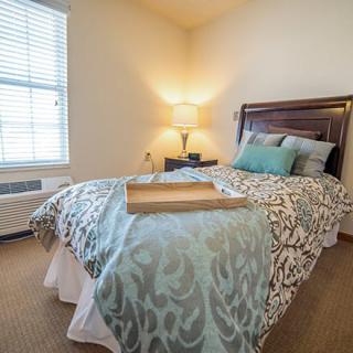 A cozy bedroom with a neatly made bed, decorative pillows, and a bedside lamp.