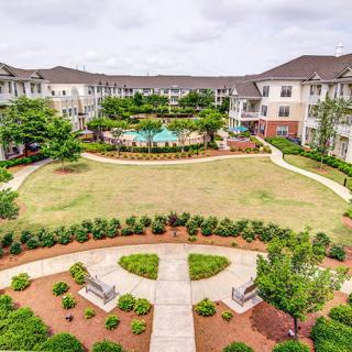 Aerial view of an apartment complex featuring a central courtyard with landscaped gardens and a swimming pool.