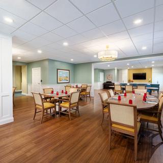 A spacious and well-lit dining room with elegantly arranged tables and chairs, featuring a wooden floor and ceiling lights.
