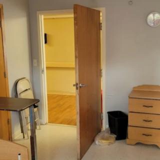 A simple room with an open wooden door, a dresser, and a metal folding chair.