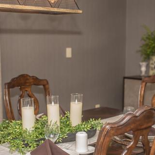 A cozy dining room setup featuring a wooden table adorned with candles and greenery under soft lighting.