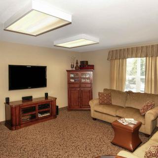 A cozy living room with a TV and sofa set, featuring warm lighting and carpeted flooring.
