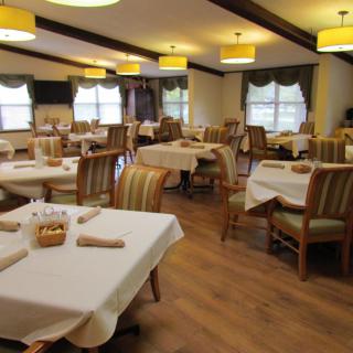 A cozy dining room with neatly arranged tables and chairs, illuminated by overhead lighting.