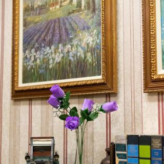 A cozy interior featuring a vase with purple flowers, framed paintings on the wall, and books arranged neatly.