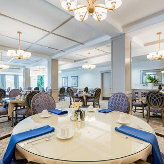 An elegant dining area with round tables, blue-accented chairs, and chandeliers.