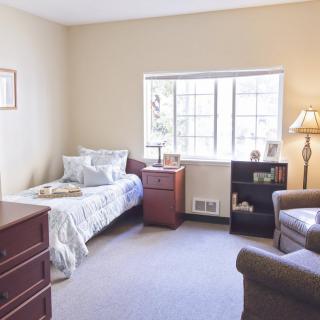 A cozy bedroom with a single bed, dresser, chair, and a window letting in natural light.