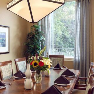 A well-set dining room table with floral centerpiece and elegant napkins, next to a large window with curtains.