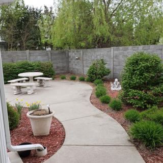 A peaceful garden patio area with a curved walkway, surrounded by greenery and outdoor seating.